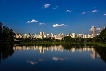 Fototapeta premium The iconic Sao Paulo skyline is perfectly reflected in the tranquil lake of Ibirapuera Park. This image highlights the contrast between the bustling metropolis and its vital urban green oasis. 