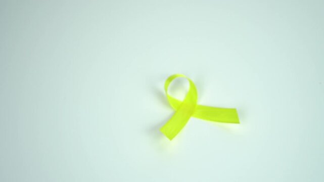 A woman's hand is holding a yellow ribbon symbolizing awareness and support for Sarcoma or Bone Cancers, Bladder Cancer, isolated on a white background