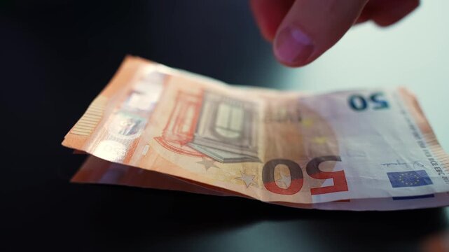 Hand places a stack of 50 euro banknotes on a dark table in close-up, showing cash payment, budgeting, savings, and business expense concept.