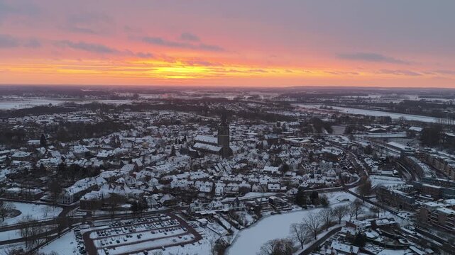 Drone view of Doesburg at dawn with golden sunlight reflecting on snowy rooftops and surrounding fields.