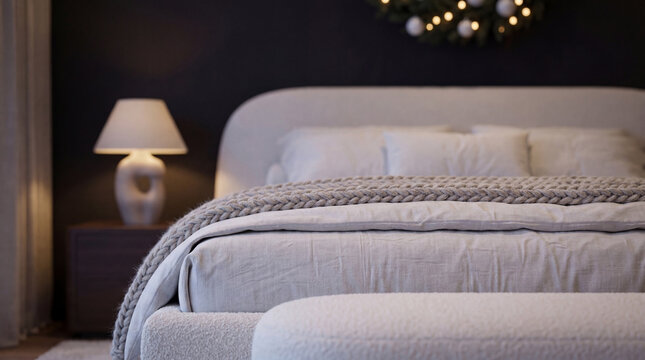 Detailed view of soft knitted blankets and plush bedding in a modern Scandinavian holiday bedroom, with a warm lamp and festive decor glowing in the background