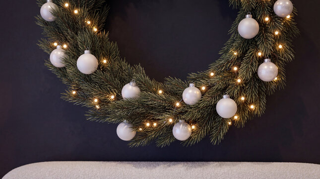 Detailed interior shot of a beautiful holiday wreath with warm lights and white decorations mounted on a dark accent wall in a modern Scandinavian bedroom