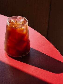 Iced Coffee Glass with Dramatic Shadow on Red Leather Cafe Table