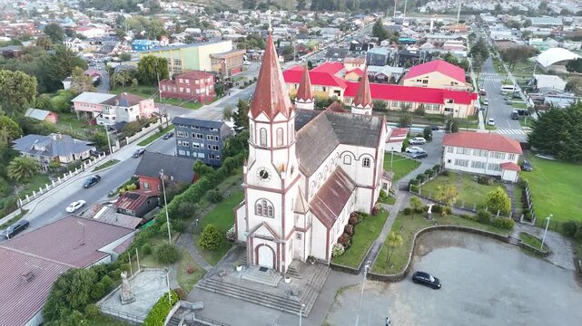 Cinematic aerial footage circling the iconic Sacred Heart Church (Iglesia del Sagrado Coraz&oacute;n de Jes&uacute;s) in Puerto Varas, Chile, showcasing its red spires and German-influenced architecture