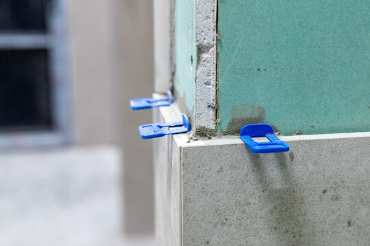 Close-up of tile leveling clips applied to a corner of a green moisture-resistant drywall partition during renovation.
