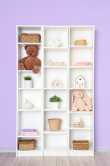 Naklejka premium Bookshelf with toys and plants near lilac wall in room