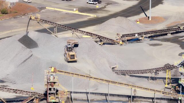 Aerial orbit of front loader working beside conveyor system in quarry