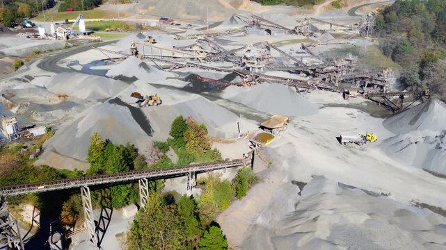 Aerial establishing backdrop of quarry operations and gravel mounds with semi truck and front loaders operating below conveyor belts