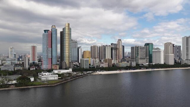 Aerial view showing the modern downtown manila skyline with its prominent skyscrapers and buildings fronting the famous baywalk and the calm waters of the bay under a cloudy sky