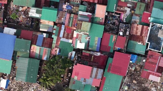 High altitude aerial view slowly gliding over a dense slum of colorful, rusted corrugated tin roofs, revealing crowded homes, narrow alleys and stark urban poverty and inequality