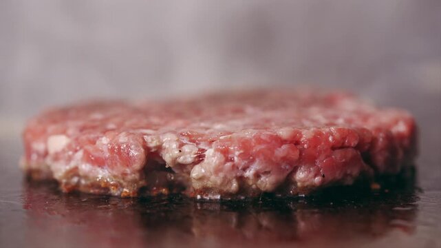 A high quality shot of a delicious pink juicy sizzling beef patty being grilled or fried on a stovetop or cooktop in a restaurant.