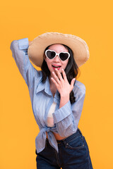 Fototapeta premium Excited Asian young woman in a sun hat and glasses to travel on holidays isolated on yellow copy space background. Travel, summer vacation, beach leisure concept.