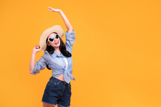 Excited Asian young woman in a sun hat and glasses to travel on holidays isolated on yellow copy space background. Travel, summer vacation, beach leisure concept.