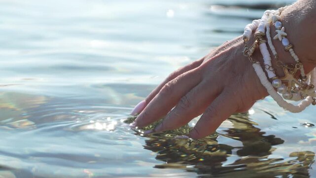 Hand water touch sparkling clear lake surface wearing beach shell bracelets during summer vacation