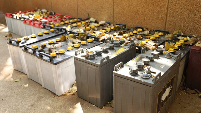 Old battery. Several worn-out truck batteries wait for recycling at a temporary outdoor storage yard next to a metal recycling wall with selective focus.