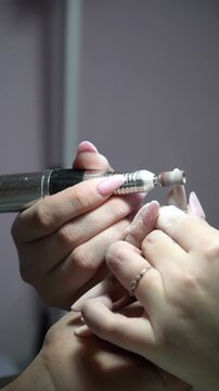 A manicurist uses an electric nail file to file a client's nail during a manicure.  Manicure master doing manicure for client with a Electric Nail File Drill Machine.  Vertical shot