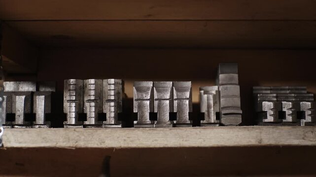 Close up of heavy metal lathe chuck jaws and machining step blocks neatly arranged in a row on a wooden workshop shelf.