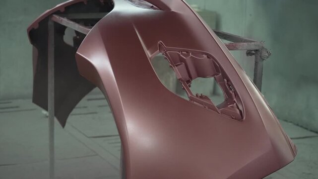 The mechanic is spraying a car bumper at a car repair shop. engineer, land vehicle, car repair shop, small business.