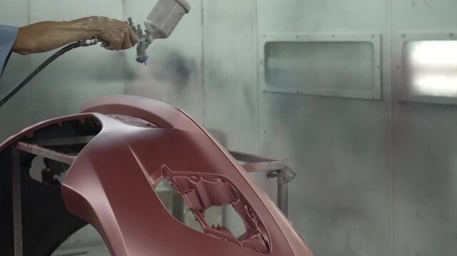 The mechanic is spraying a car bumper at a car repair shop. engineer, land vehicle, car repair shop, small business.