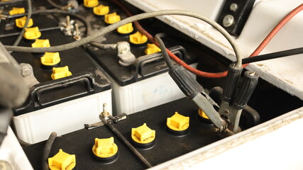 Battery terminal clamp. Close-up of black charging cable clamps attached to redundant battery terminals for golf cart battery charging and selective focus maintenance concept. © kanin