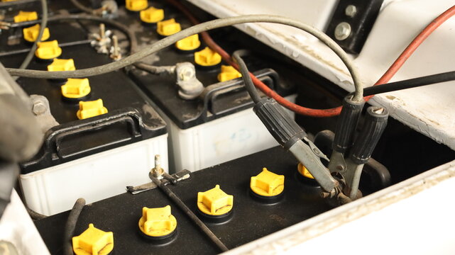 Battery terminal clamp. Close-up of black charging cable clamps attached to redundant battery terminals for golf cart battery charging and selective focus maintenance concept.
