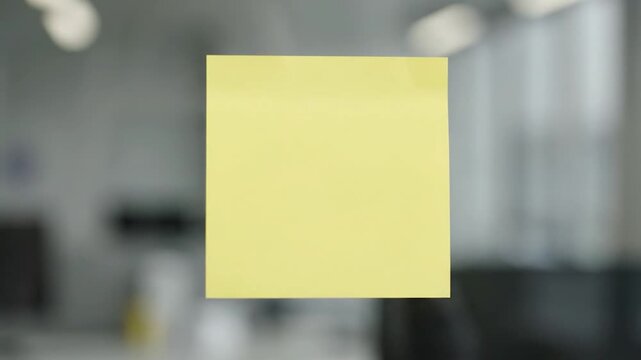 Yellow Sticky Note Attached to Glass Surface in Office Environment.