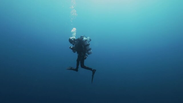 Silhouettes of scuba divers ascending toward the ocean surface in the Red Sea. Sunlight filters through clear blue water as the divers slowly rise, creating a dramatic underwater scene.