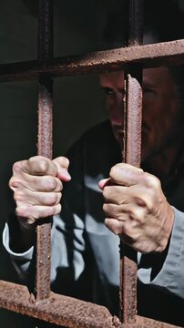 Angry prisoner shaking jail bars and screaming in frustration inside prison cell