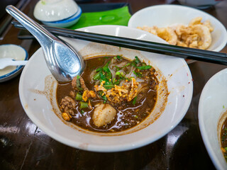 Traditional Thai boat noodles with thick spicy pork broth, meatballs, and liver in ceramic bowl with chopsticks