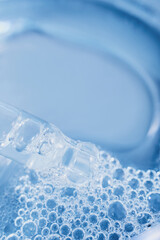 Clear cosmetic liquid dripping from dropper onto blue water bubbles, symbolizing skincare treatment
