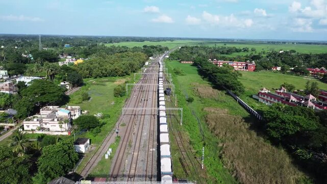Aerial view of a long indian freight train transporting cargo through rural India. Indian train traveling on a straight track. Indian railway transportation. Indian transport concept. 