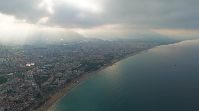 Alanya, Turkey. Aerial drone shot of urban coastline with Oba Beach, Tosmur Beach and sun rays through clouds over mountains and sea.. Aerial View