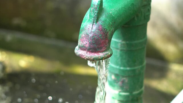 Close up of water flowing from a green manual hand pump in rural India. 