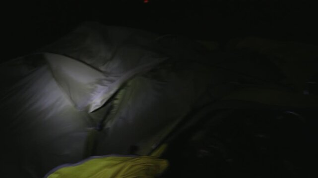 Interior tent illuminated by headlamp during winter night camping, rough winds blow and spread gear everywhere in panic