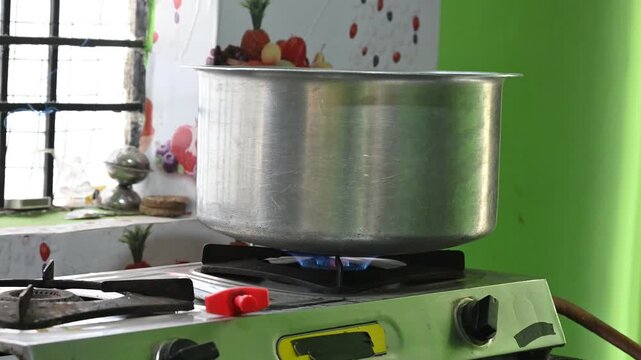A rural Indian woman cooking on an LPG gas stove in a simple kitchen. The image highlights rising cooking gas prices, energy crisis