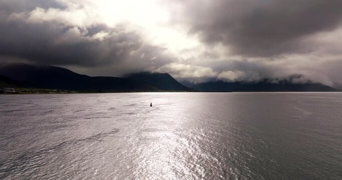 Aerial dolly to sailboat off coastline below dark mountains in Sortland Vesteralen Norway