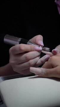 Removal of old gel from nails in the salon. Manicure master doing manicure for client with a Electric Nail File Drill Machine.  Vertical shot