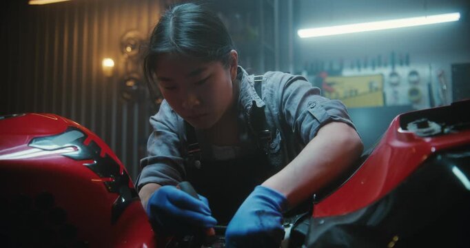 In Modern Garage, Determined Young Female Mechanic Uses Screwdriver to Neatly Position Electronic Wiring Inside Motorcycle. Concept of Craftsmanship, Technical Precision, Independent Bike Maintenance.