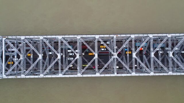Top down aerial view of vehicles moving across a steel truss bridge. Modern steel bridge construction and transport. Massive steel truss bridge spanning a wide river.