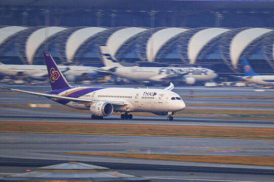 30-01-2026, Bangkok Thailand, Thai Airway airplane with purple and gold tail is landing on runway at airport, with modern terminal in background. 