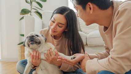 Asian couple playing with pug dog together at home