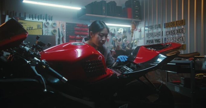 Woman in Grey Uniform and Blue Protective Gloves Performs Delicate Repair on Red Sport Motorcycle. Using Manual Screwdriver, Carefully Unscrews Bolts Access Battery and Electronic Wiring Under Seat.