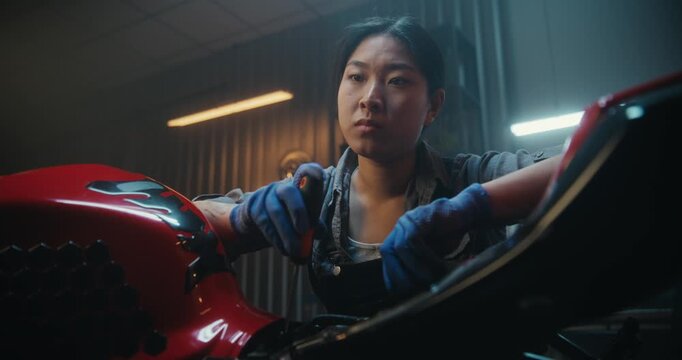 In Garage, Young Mechanic Pauses Beside Motorcycle, Thinking Intensely About How Fix Malfunction. Woman Massaging Stiff Neck After Long Hours Troubleshooting. Problem Solving, Technical Challenge.