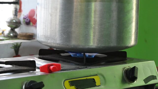 A rural Indian woman cooking on an LPG gas stove in a simple kitchen. The image highlights rising cooking gas prices, energy crisis