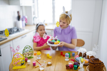 Fototapeta premium A mother and daughter enjoy decorating Easter eggs together in a bright kitchen, surrounded by festive decorations and cakes