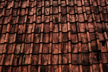 Top-view pattern of aged clay roof tiles. Dark orange weathered texture for rustic architecture and urban heritage backgrounds. © EkoPriyatno