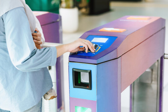 Muslim woman using a contactless credit card to pass through an automated public transport fare gate in a bright, modern station