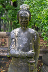 Fototapeta premium A stone statue of a mandarin stands in the Mausoleum of Emperor Dong Khanh, Hue, Vietnam., a popular tourist destination, The statue is covered in moss and lichen.