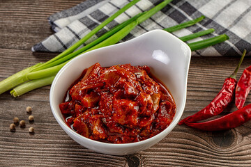 Spicy red chili pickle in a white bowl on a rustic wooden table with fresh ingredients