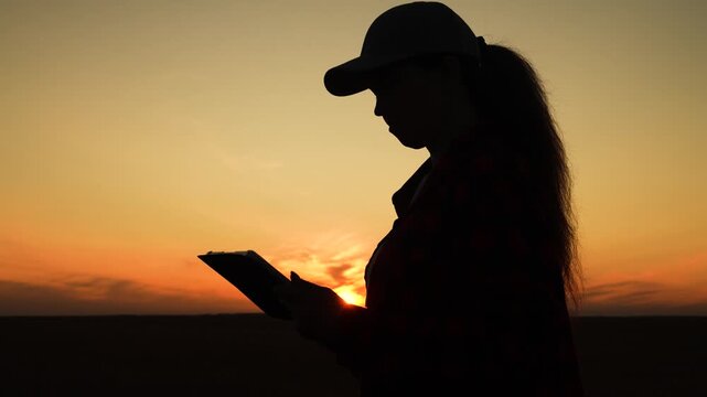 Silhouette woman working digital tablet, young girl sunset, human journey digital technology, golden hour light outlines a person planning or learning in the field., field researcher collecting notes